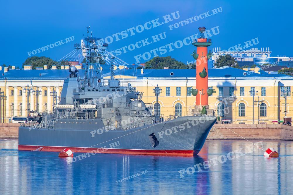 Фотография показывает военный корабль на фоне Ростральных колонн в Санкт-Петербурге. Это изображение может быть использовано для иллюстрации военно-морской тематики, в туристических проспектах, в образовательных материалах о городских достопримечательностях или как часть выставки, посвященной военно-морскому флоту России.